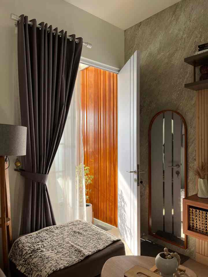 Natural-toned entrance space featuring wooden panels, an arched mirror, dark curtains, and an armchair creating a cozy atmosphere