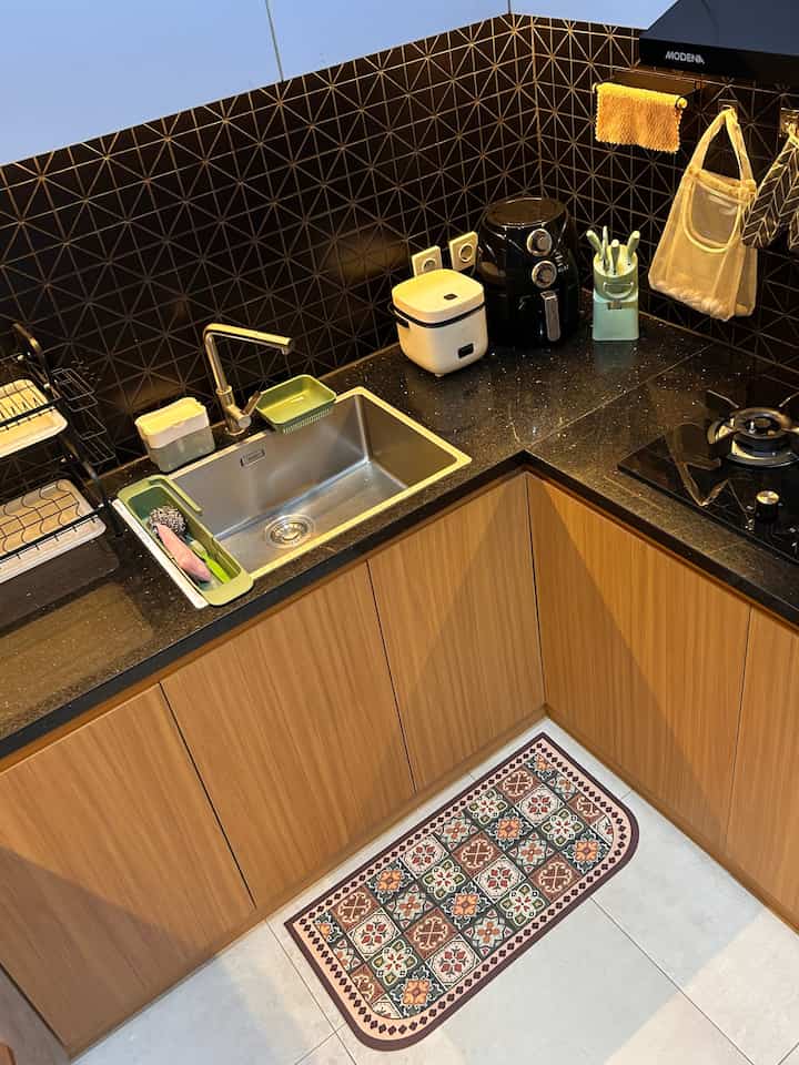 Compact kitchen space featuring black tiled backsplash, wood-tone lower cabinets, sink and kitchen accessories
