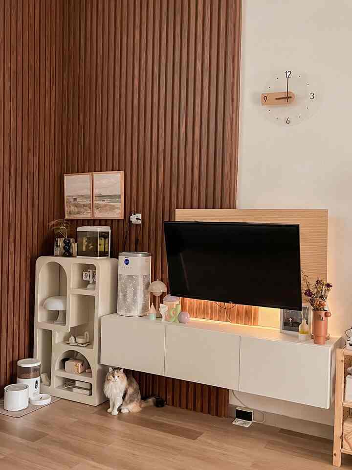 Warm living room featuring natural wood tone wall panels, white TV stand, and a cat scratching post with a cat sitting on floor