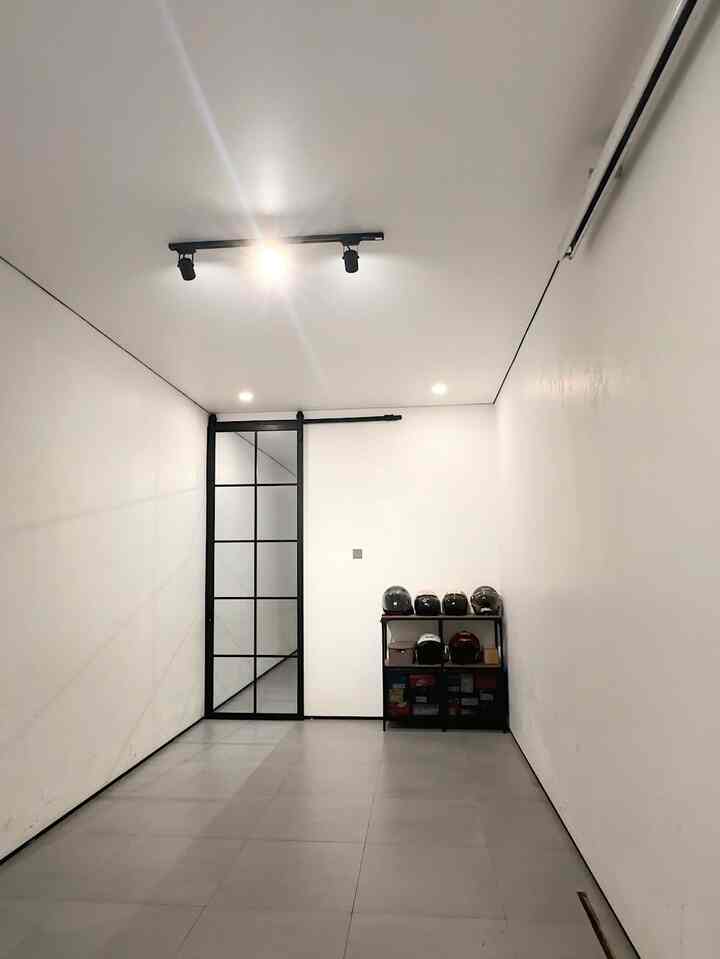 Narrow compact entrance space with white walls and ceiling, black-framed glass sliding door, and shelf with helmets arranged simply