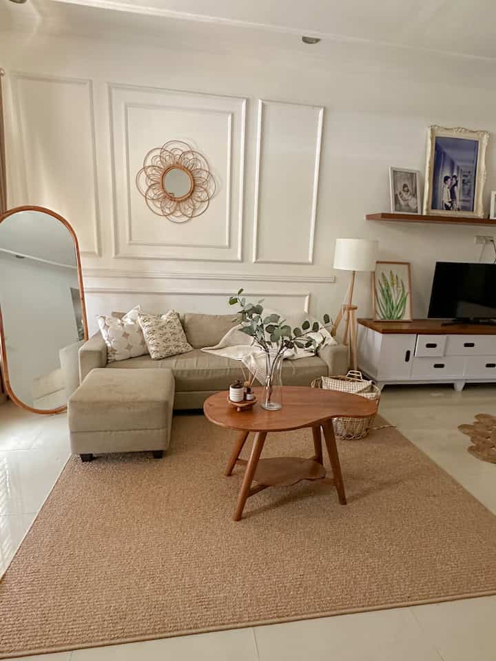Beige and wood tone living room featuring beige sofa, rug, wooden coffee table, wall moulding, and large wall mirror with cozy atmosphere