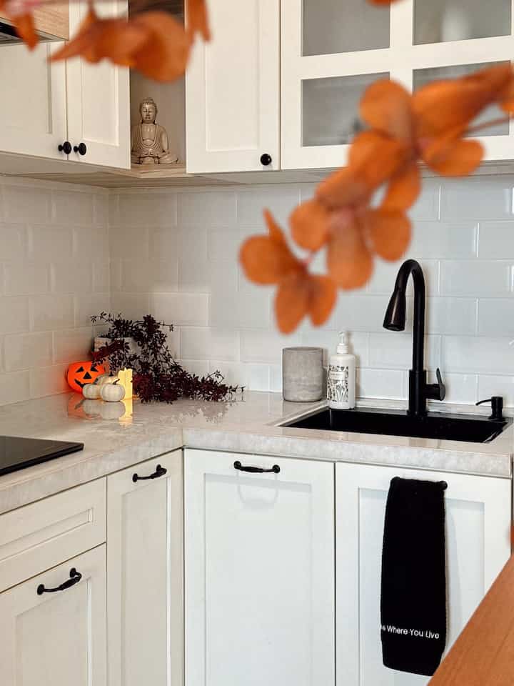 Clean kitchen corner with white tiles and black faucet, cozy space featuring Halloween decoration on countertop
