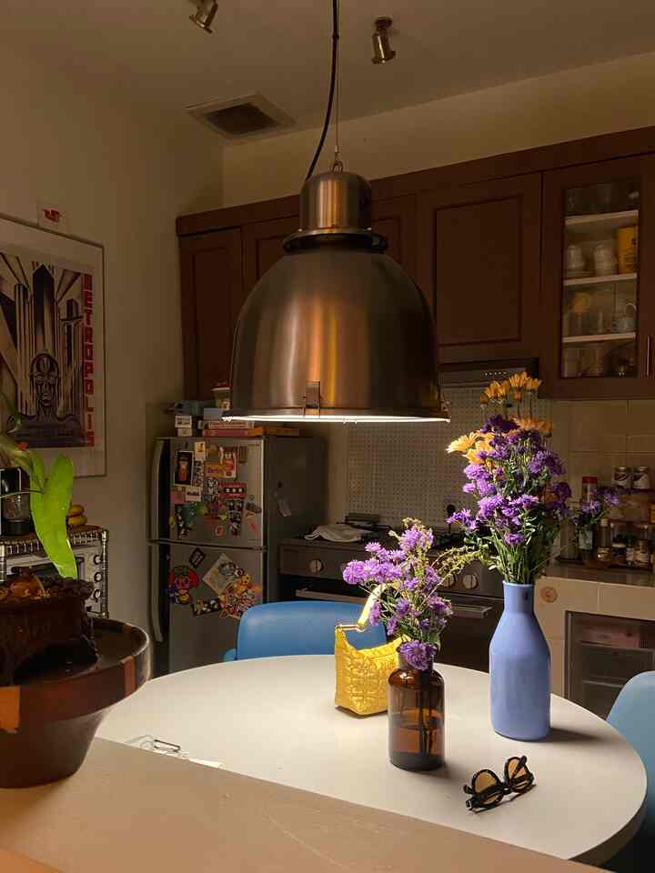 Warm-toned kitchen and dining room featuring a white round dining table, blue dining chairs, and a metallic pendant light creating a cozy atmosphere