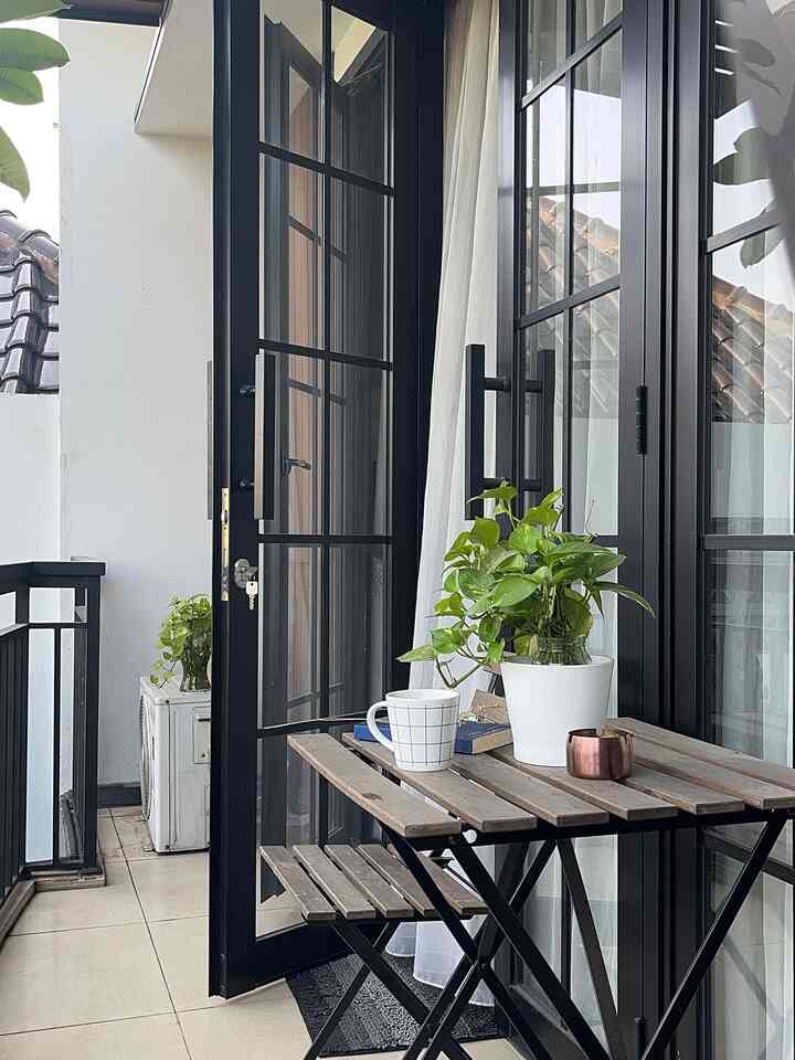 Black and white toned balcony featuring wooden table and chair with a green plant, creating a cozy outdoor space