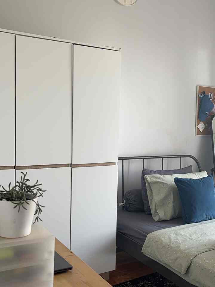 Compact bedroom featuring white wardrobe and gray bed with blue cushions, creating a modern and neat atmosphere