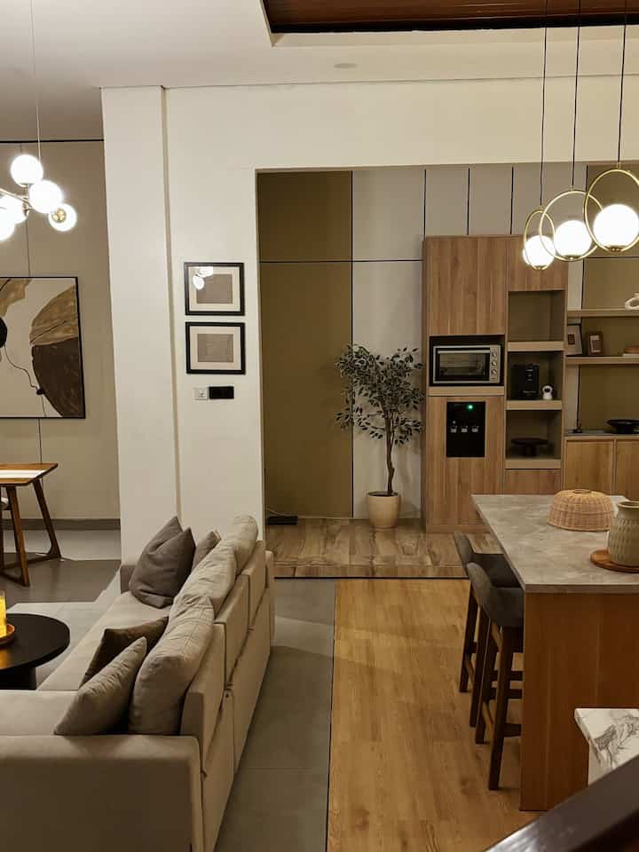 Light brown and white toned living and dining room featuring beige sofa bed and pendant lights in a modern natural space