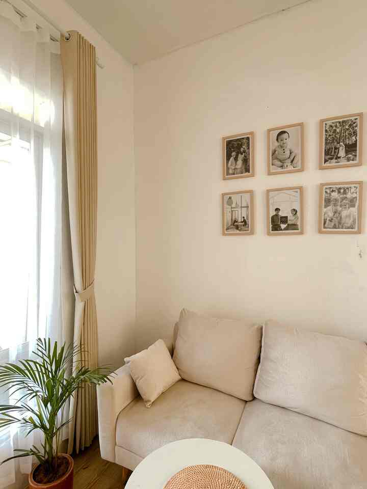 Beige and white toned living room featuring simple sofa, curtains, and family photo frames in a natural modern space