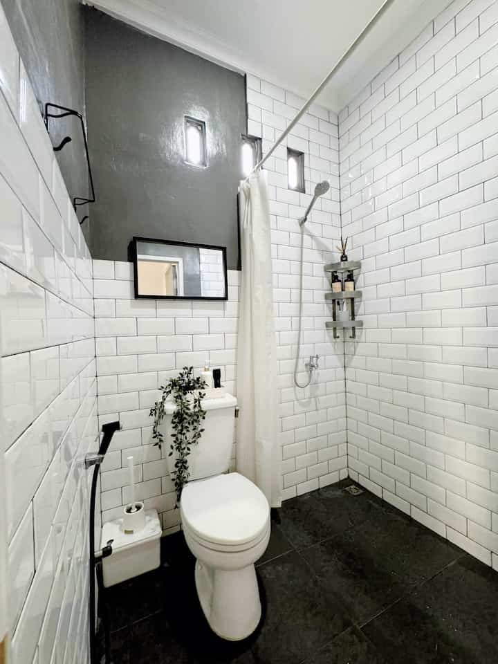 Compact bathroom in white and black tones featuring multi-tier corner storage and a shower curtain for a clean space