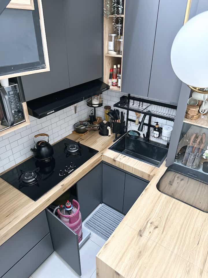 Compact modern kitchen with gray and wood tones featuring black sink, gas stove, and efficient storage racks