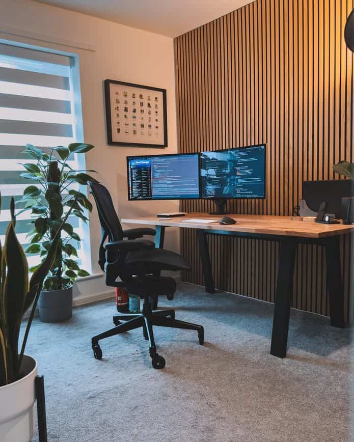 Simple modern home office featuring wood tone wall panel, desk, and blinds with a cozy atmosphere