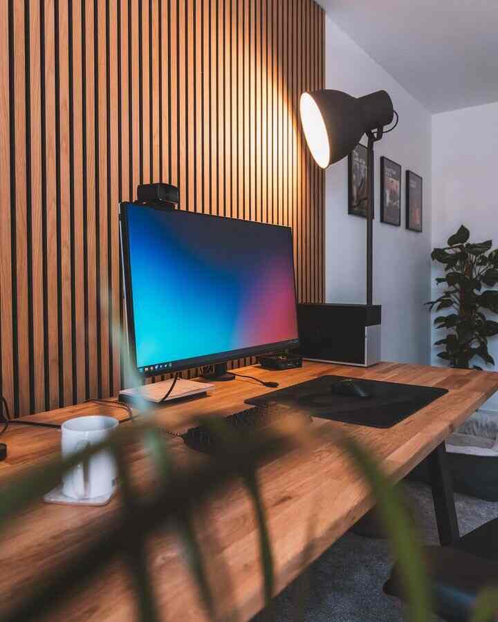 Wood tone and gray home office featuring a modern clean desk with computer and desk lamp