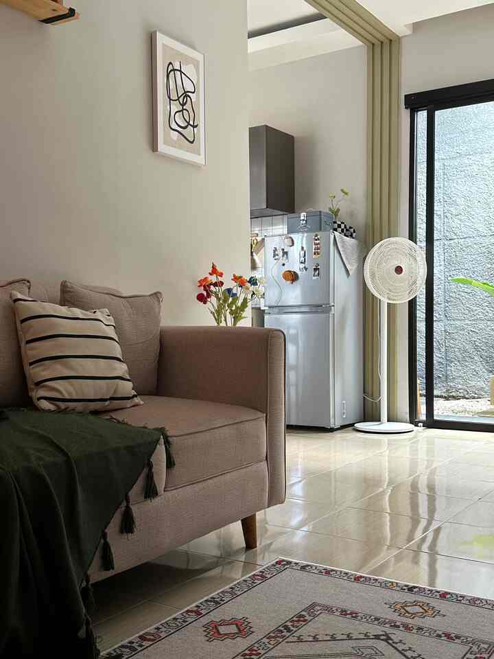 Beige and white toned living room featuring a beige sofa and visible kitchen area, creating a cozy natural atmosphere