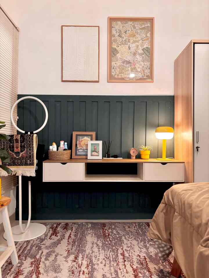 Cozy single bedroom with navy wall panel, beige bedding, a wooden desk, and a yellow table lamp