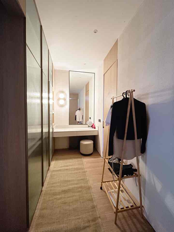 Ivory and wood-tone walk-in closet featuring a long corridor with a vanity table and wooden clothes rack in a modern natural style