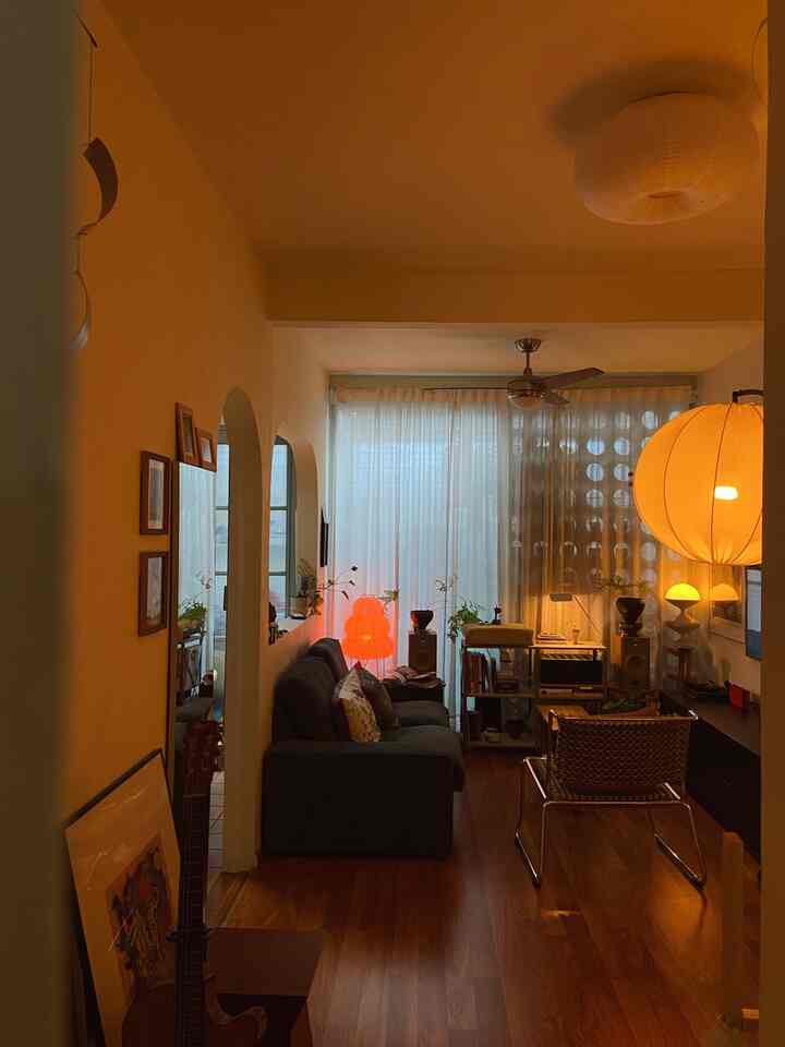 Cozy living room with natural wood flooring, dark sofa, pendant lighting, and sheer curtains creating warm ambiance