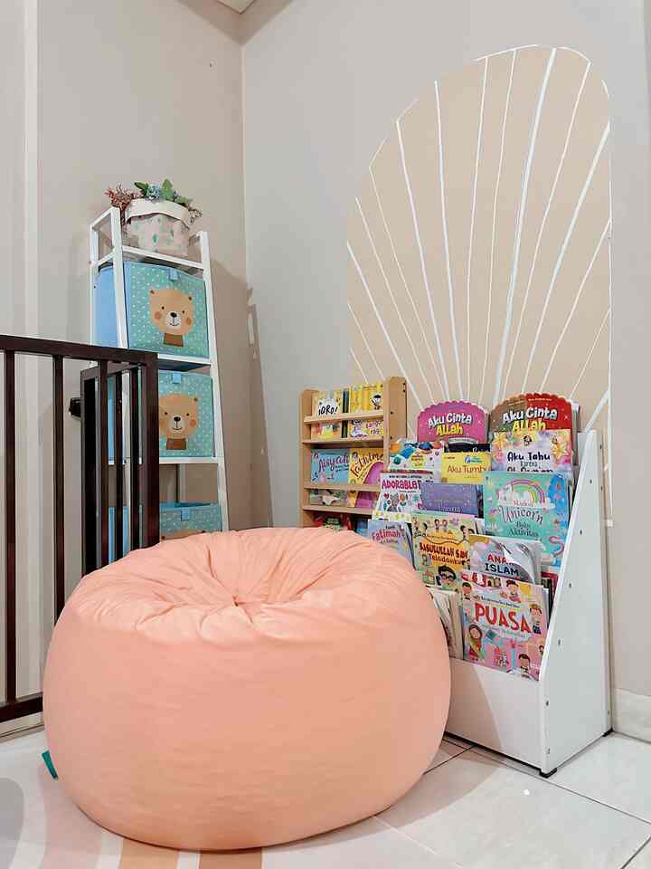 White and soft peach toned kids' room featuring a bookshelf filled with colorful storybooks and a large peach bean bag, creating a cozy reading space