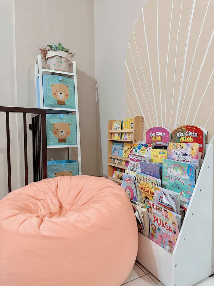 Soft pink bean bag with white walls, children's books, and toy storage in a kids' space