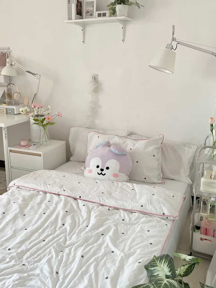 Simple bedroom with dominant white and pink accents featuring bed, cute cushion, and plants in a natural atmosphere