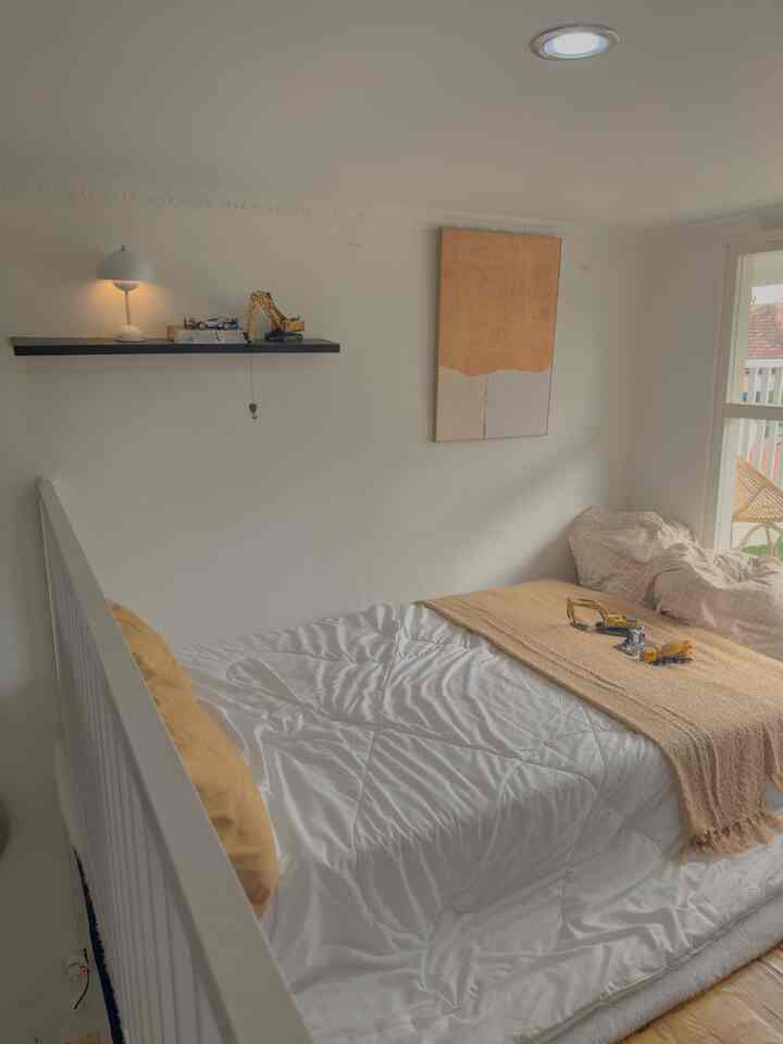 White and beige toned mezzanine bedroom featuring a large window and simple wall art creating a cozy atmosphere