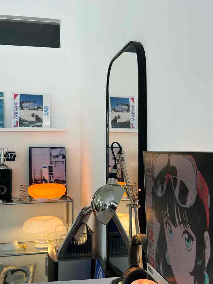 White-walled space featuring a silver table lamp and black-framed standing mirror with a modern home office vibe