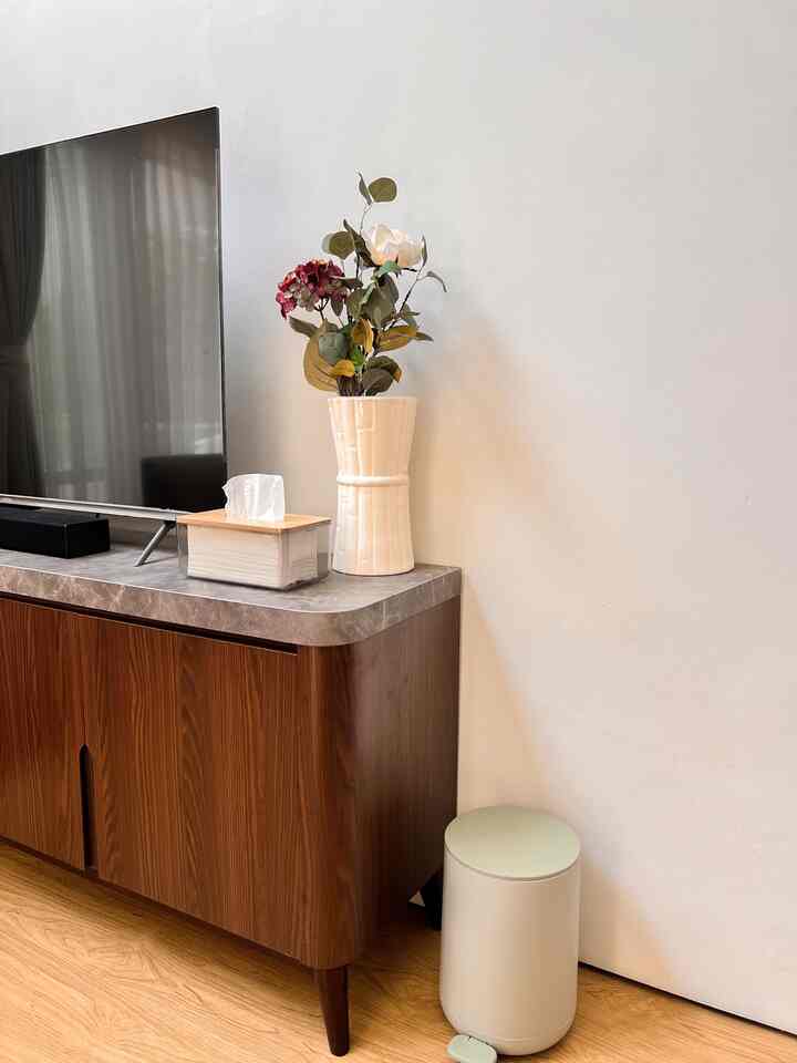 Bright white-walled living room featuring a wood-tone TV stand with a flower vase and tissue box on top, creating a clean atmosphere