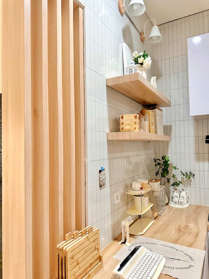 Natural wood tones and white tiles create a harmonious kitchen space featuring a wooden table and storage shelves with a clean atmosphere