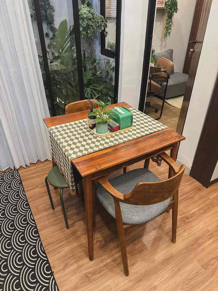 Natural wood-toned dining room for two featuring a checkered table runner, plants near window creating cozy atmosphere