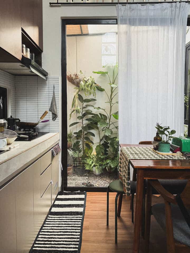Light brown vinyl floor kitchen space with dark brown dining table, greenery by window and white curtains creating a warm natural atmosphere