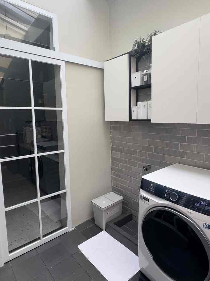 White and gray toned long narrow laundry space featuring wall cabinets and a washing machine with a clean and functional atmosphere