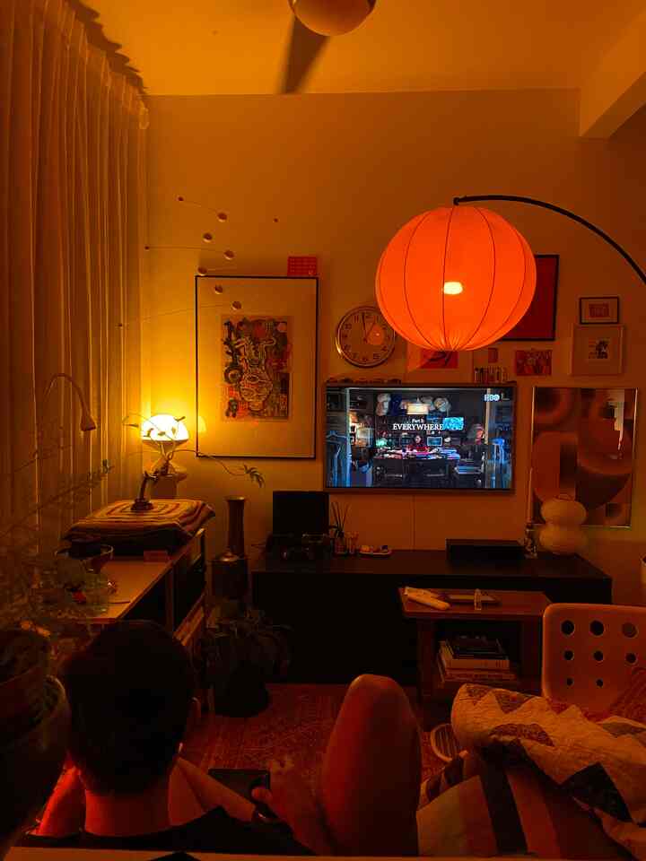Orange-toned warm lighting living room featuring central TV, multiple framed artworks, and a cozy sofa arrangement