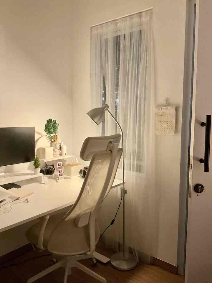 White and brown toned home office space featuring simple furniture and floor lamp with cozy work environment