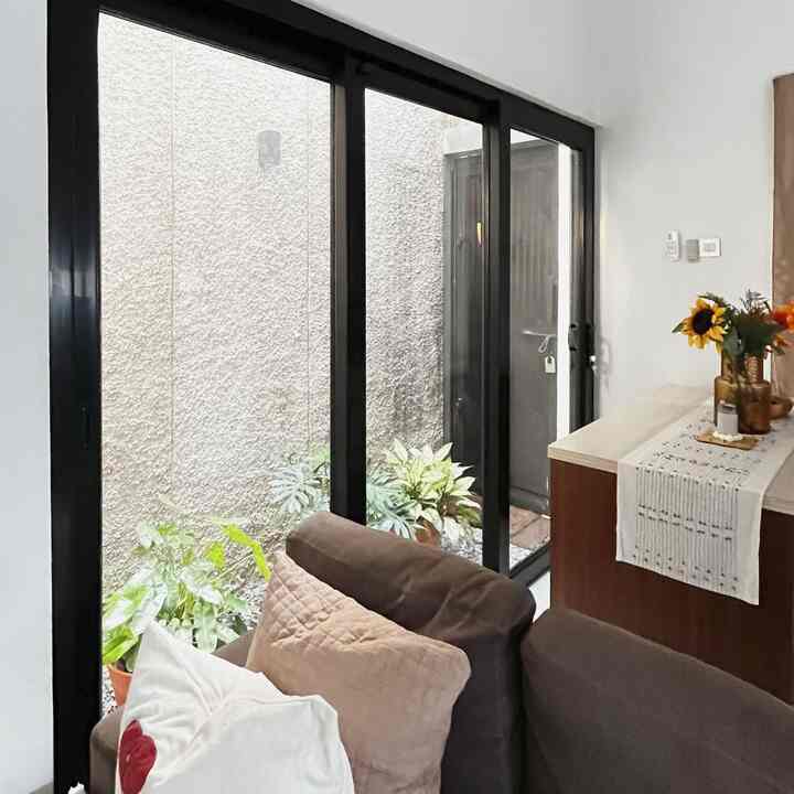 Brown sofa and plants in a natural-toned living room featuring a balcony with an inviting atmosphere