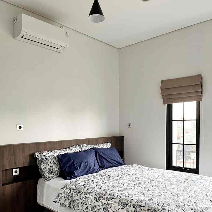 Modern bedroom with white walls and navy pillows, featuring a wooden bed frame and beige blackout curtain creating a calm atmosphere