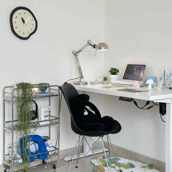White-toned small home office desk corner featuring a modern black office chair and plants in a simple setting