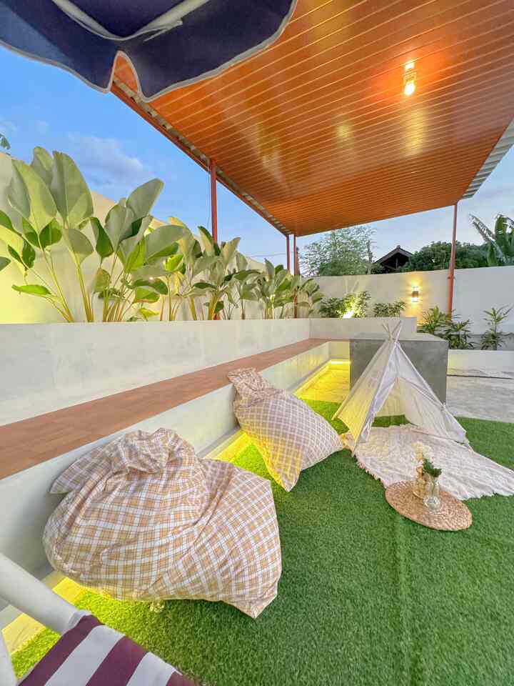 Green artificial grass with beige bean bags and a white teepee tent in a cozy outdoor balcony space