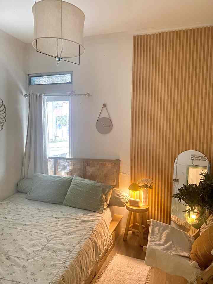 A small bedroom with bright white walls and wood tone paneling, featuring a rattan headboard and stool in a minimal, warm setting