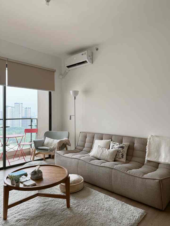 Beige-toned living room featuring a large beige sofa, teal armchair, round wooden coffee table, and a balcony with city view