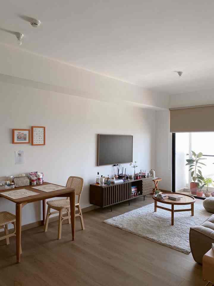 A white-walled natural-tone living and dining room featuring wooden furniture and plants with a modern, cozy atmosphere