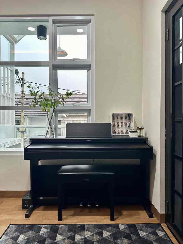 Minimal living room with black digital piano, wood tone flooring, and window providing natural light