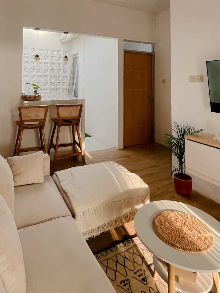 A beige and wood-tone living room featuring a cream sofa and rattan bar stools creating a cozy cafe style atmosphere