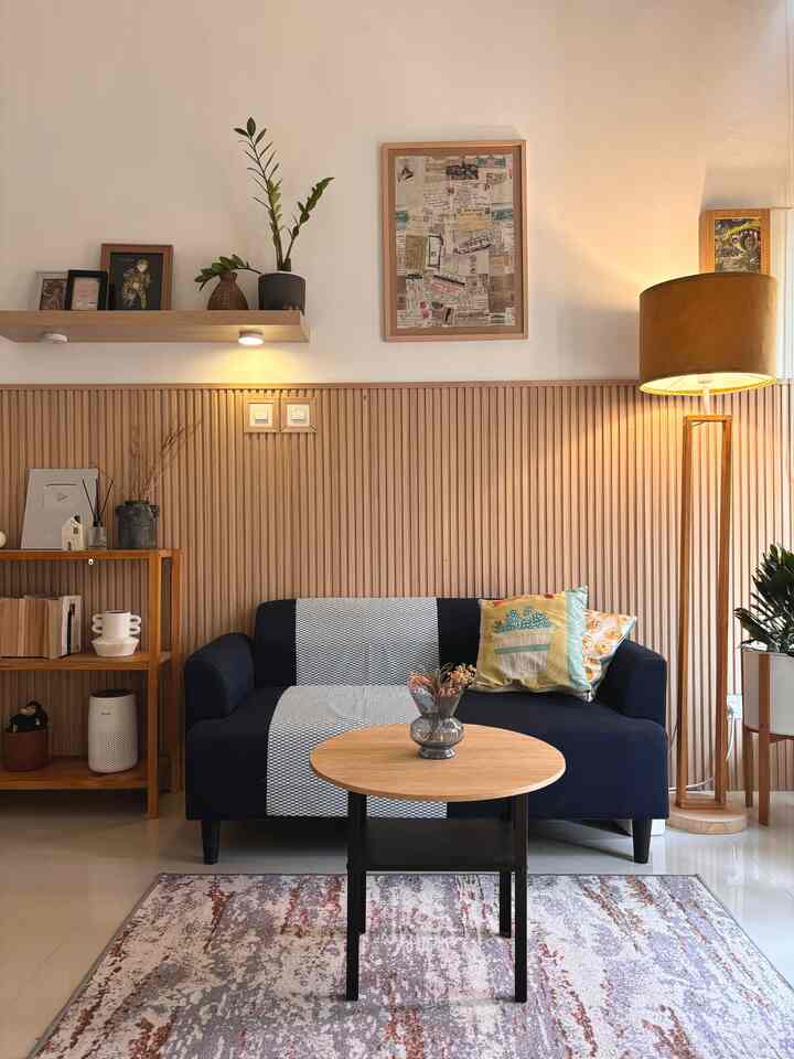 Living room with wood tone wall panels, navy sofa, round coffee table, and floor lamp creating cozy atmosphere
