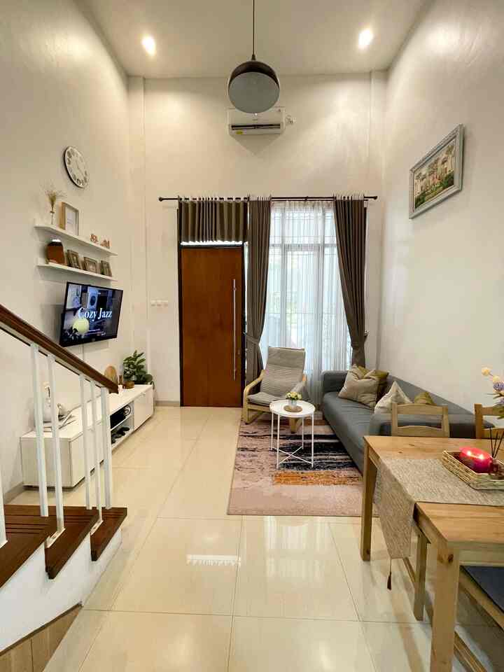 Modern living room with white walls and brown wooden accents, featuring gray sofa, armchair, pendant light, and carpet