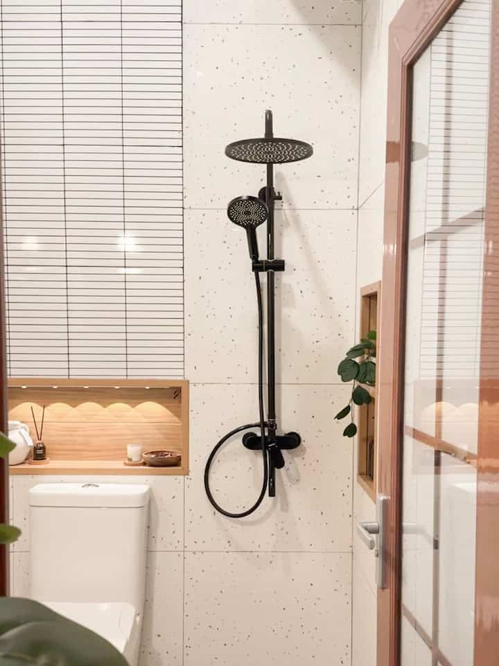 Compact bathroom in white and brown tones featuring modern black shower and arched mirror with clean design