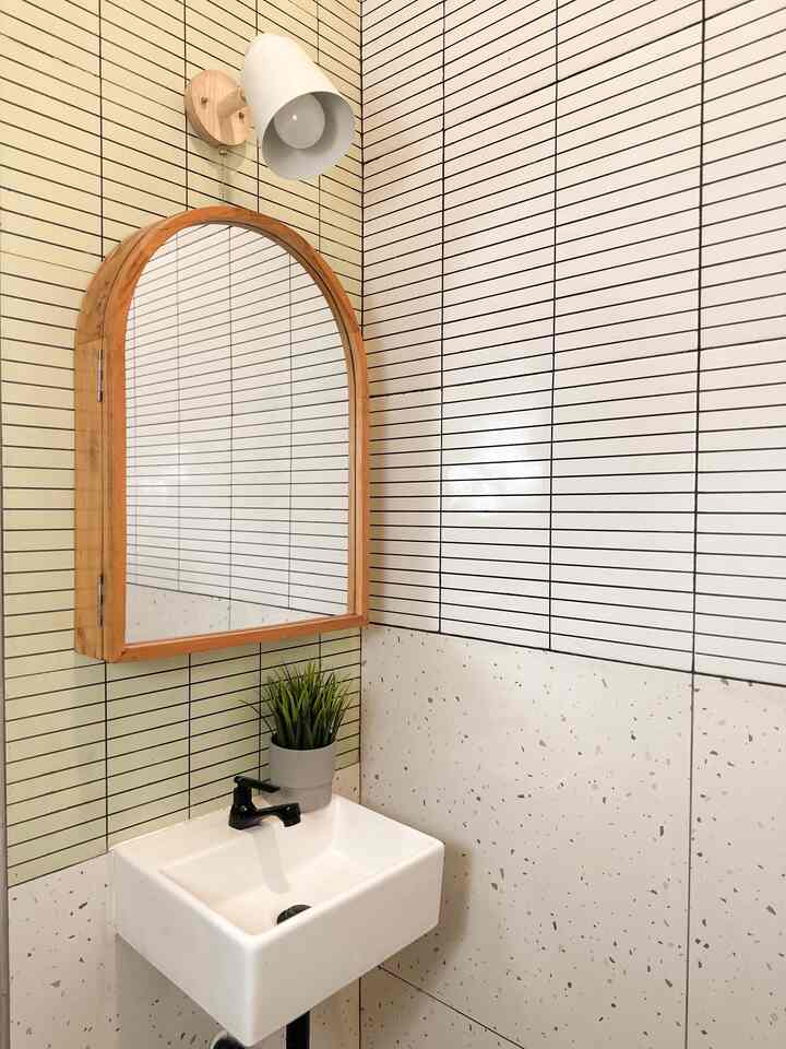 White and wood-tone bathroom featuring an arched mirror and wash basin, showcasing a clean and modern interior