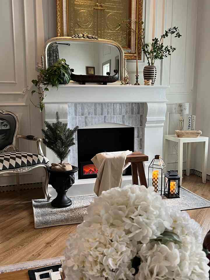 Classic living room with wood tone flooring and white fireplace, featuring artificial plants and decor creating a cozy atmosphere