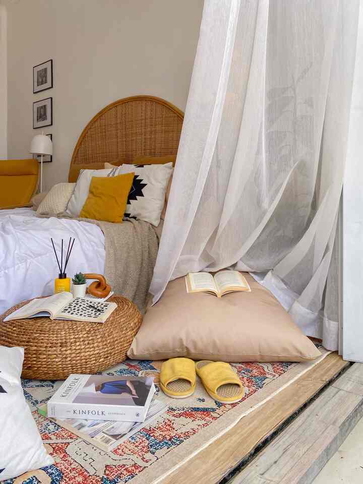 A bedroom in yellow and natural tones features a rattan headboard, cushions, and a vibrant abstract carpet, creating a cozy Boho atmosphere