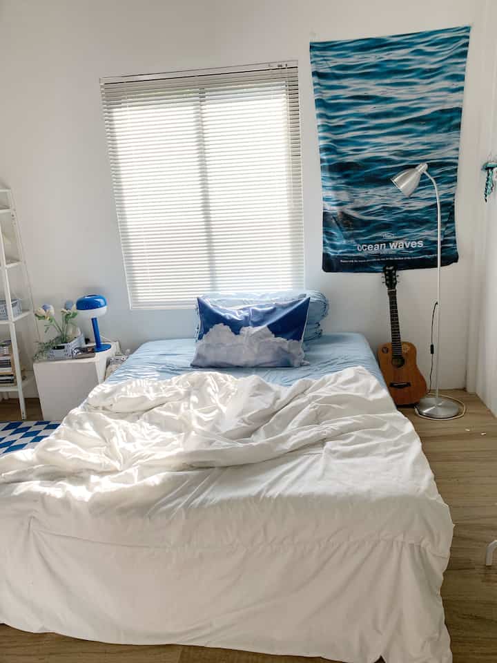 White and blue toned bedroom featuring a plush bed and ocean waves poster with natural modern style