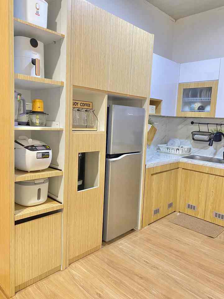 A compact kitchen featuring wood tone cabinetry and white accents, built-in storage shelves, and a silver refrigerator for a clean look