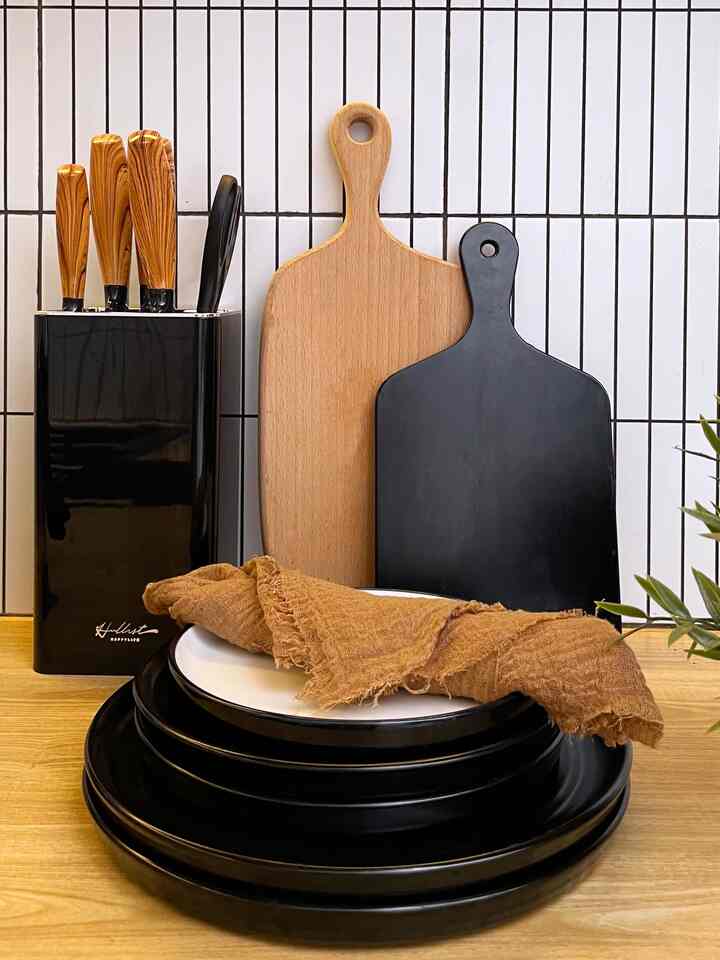 Natural and black toned kitchen space featuring cutting boards, knives, and stacked plates arranged neatly with a clean atmosphere