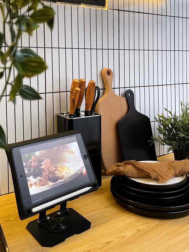 Clean kitchen space with white tiled wall and wood-tone countertop featuring knives, cutting boards, tableware, and artificial plant